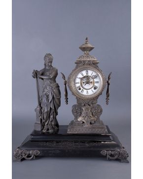 402-Antigua guarnición decorativa compuesta por reloj de sobremesa inglés y escultura de dama con arpa en metal sobre base pintada en negro. Esfera con nu