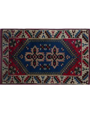 877-Alfombra turca. estilo caucasiano. de lana anudada a mano. con campo central en azul . fondo rojo y contorneada con una greca.