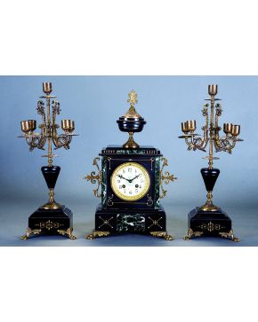 773-Reloj con guarnición en mármol negro y bronce dorado. Francia. C. 1900. Reloj con esfera de porcelana blanca. numeración romana en negro y remate en f