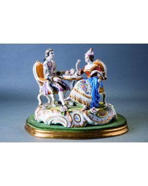 802-Grupo en porcelana polícroma centroeuropea representando una escena galante con pareja tomando el té sobre base decorada con rocallas y flores. c. 190
