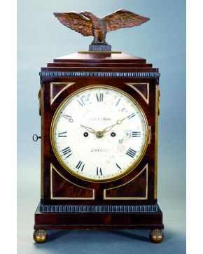 735-Reloj de mesa inglés con caja en madera coronada por un águila en bulto redondo. Esfera en porcelana blanca con numeración romana en negro firmada Tha