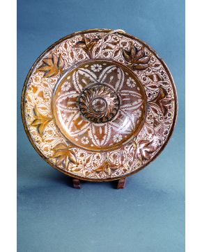 1149-Plato en cerámica de reflejo metálico de Manises. s. XVI. Decoración vegetal de trifolios y flores en relieve en el alero. Asiento con umbo helicoidal