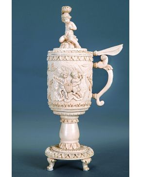 1337-Tankard alemán en marfil tallado con elementos alegóricos referentes al vino y al dios Baco. Remate con figura de niño con cesto de uvas sobre la cabe