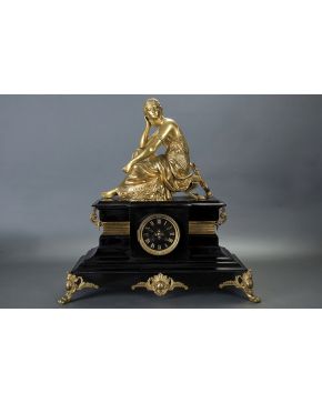 719-Reloj de sobremesa francés con peana en mármol negro y figura en bronce dorado de odalisca con lira en la parte superior. Esfera negra con numeración 