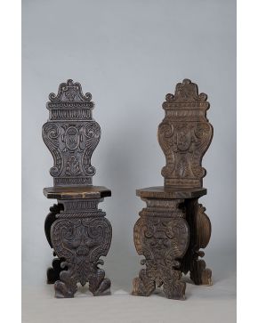477-Pareja de sillas gallegas populares en madera tallada con dos patas profusamente talladas en forma de medallón unidas por chamabrana.
