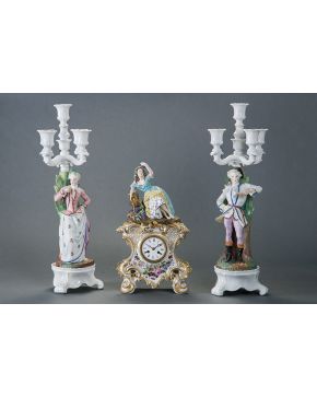 724-Lote formado por reloj de sobremesa estilo isabelino en porcelana esmaltada con decoración de flores y remate de bacante; y pareja de candelabros de c