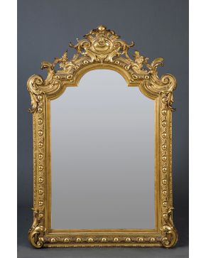 682-Gran espejo en madera tallada y dorada con decoración relevada de ovas en el perímetro. hojas de acanto en las esquinas y copete vegetal calado con fl