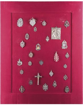 709-Panel en plata y plateado con 27 colgantes antiguos de distintas advocaciones. una placa devocional con la Adoración en relieve. y un amuleto en filig