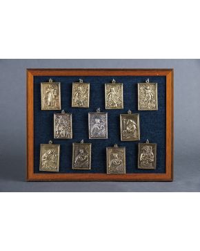 647-Lote formado por 11 placas devocionales antiguas de distintas advocaciones en bronce dorado y una en plata. Enmarcadas.