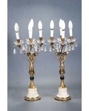 389-Pareja de candelabros de cuatro luces estilo Imperio. con decoración de lágrimas de cristal y platillos. y fuste de figura alada. Sobre peanas en márm