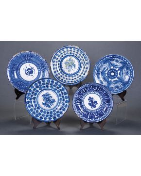 485-Lote de cinco platos en cerámica de Manises con decoración azul y blanca de flores y hojas. Uno firmado F.S.. Tres de ellos restaurados. Piquetes.