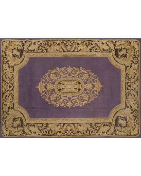 871-Alfombra en lana de nudo español. Con marcas M. STUYCK. Elegante diseño de roleos en dorado y óvalo central con motivos vegetales sobre campo morado.