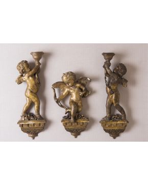 599-Lote de tres esculturas de adosar en madera tallada y dorada. S. XIX. Una de ellas Cupido y pareja de angelitos torcheros. Consolidaciones y faltas. 