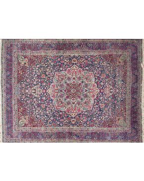 359-Alfombra persa con gran rosetón polilobulado central y profusa decoración vegetal y floral sobre campo granate y azul. Colores complementarios: rojo. 