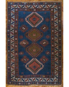 1060-Alfombra persa con decoración de motivos decorativos romboidales sobre campo azul y triple cenefa perimetral con motivos geométricos. Algún desgaste.