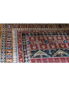 1051-Alfombra persa en lana con decoración de motivos geométricos sobre campo granate. Colores complementarios: azul. negro y amarillo. Faltas y desgastes.