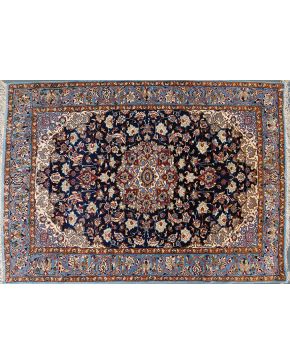 1206-Alfombra persa Ispaham en lana con profusa decoración de motivos vegetales y florales con lóbulo central sobre campo azul.