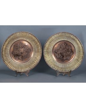 1009-Pareja de grandes platos decorativos orientales en cobre con ala trenzada en metal. Uno con decoración en relieve de paisaje y otro con ave. Con sello