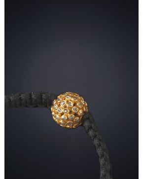 573-PULSERA CON ESFERA DE BRILLANTES. sobre una montura de oro amarillo de 18k y cordón de seda negro.