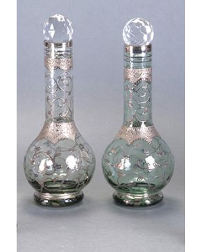 1187-Pareja de antiguos catavinos en vidrio incoloro con decoración en tonos platas. Tapones mordernos en cristal facetado. Con iniciales en la base.