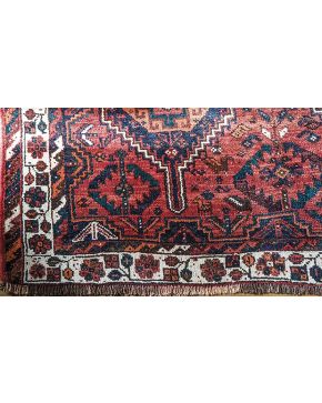 719-Alfombra persa en lana con decoración de motivos geométricos sobre campo granate. con cenefa floral sobre campo beige.