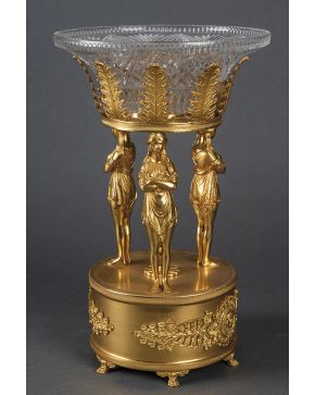 1027-Centro francés estilo Imperio. En bronce dorado con la representación de tres cariátides que sujetan el recipiente en cristal moldeado posterior. Base