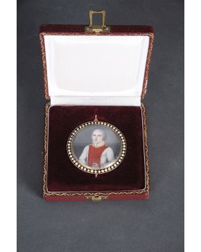 853-Importante guardapelo con miniatura circular representando un retrato de caballero. Con montura en metal dorado orlado de perlas. En su estuche origin