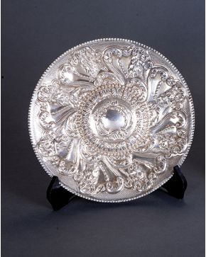 1022-Bandeja circular en plata española punzonada profusamente cincelada con motivos vegetales  y umbo relevado. Perímetro acanalado. Marcas de Durán. Madr