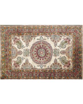 905-Alfombra persa en lana y seda con medallón central y decoración vegetal y floral sobre campo beige y cenefa en tonos verdes y ocres. Color complementa