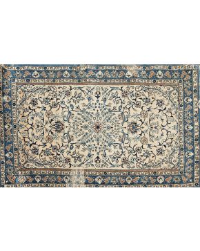 582-Alfombra persa en lana y seda con decoración vegetal sobre campo beige y cenefa en azul. Faltas.