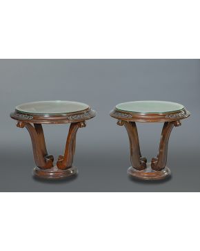 551-Lote de dos mesas circulares auxiliares en madera tallada. Pie con cuatro volutas y tapas de cristal.