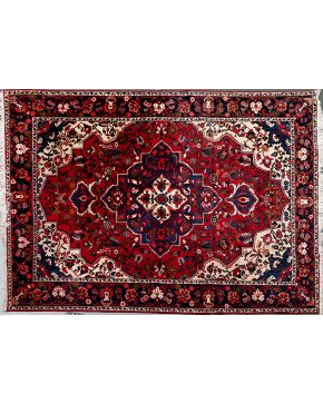 810-Alfombra persa Baktiar en lana con decoración vegetal y floral sobre campo granate y medallón central polilobulado sobre campo azul oscuro.