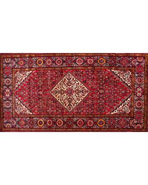 1168-Alfombra persa en lana con rombo central y abigarrada decoración vegetal y floral sobre campo granate.