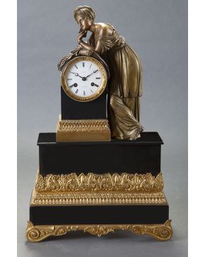 673-Reloj de sobremesa en mármol negro y bronce dorado Napoleón III Francia. mediados s. XIX. Figura femenina en bulto redondo apoyada en la esfera con ma