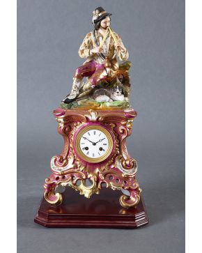 601-Reloj de sobremesa en porcelana esmaltada Francia. s.XIX. Numerado. Remate de personaje tocando una doble flauta. Sobre base de madera. 