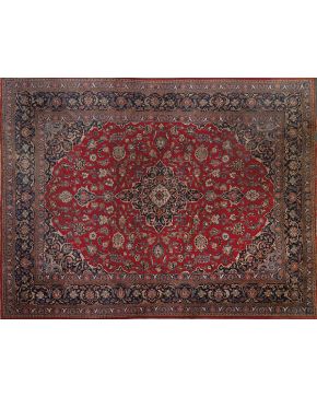 560-Elegante alfombra persa en lana sobre campo granate. Decoración vegetal. Triple cenefa. la central azul marino a juego con rosetón central y esquinas.