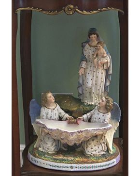 551-Decorativa benditera en biscuit policromado representando Virgen con niño y ángeles. Con marcas.
