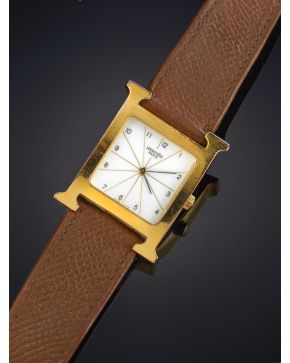 973-HERMES MODELO HEURE. Reloj de pulsera para caballero con caja en forma de H chapada en oro amarillo de 18k y correa en piel marrón. Movimiento de cu