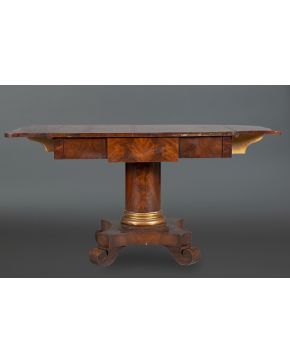 1069-Mesa de alas Carlos X en madera de palma de caoba tallada y dorada con pie a modo de columna terminada en cuatro patas de volutas. Cajón frontal.