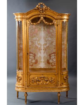 634-Elegante vitrina estilo Luis XVI en madera tallada y dorada con remate de antorchas y decoración en relieve a candelieri. Puerta central y laterales