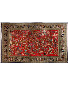 502-Alfombra persa en lana y seda con decoración vegetal sobre campo granate. Representación de árbol de la vida y animales. Cenefa en azul oscuro.