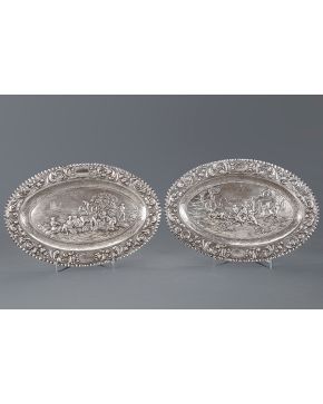 875-Pareja de bandejas ovales en plata española punzonada con perímetro acanalado y decoración cincelada y relevada con escenas de la siega y riña en l