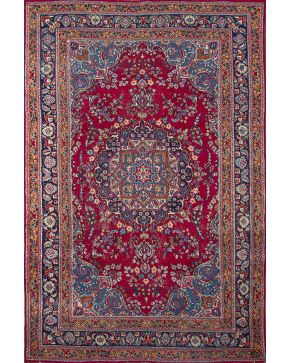 875-Alfombra persa en lana con óvalo central y decoración vegetal y floral sobre campo granate y cenefas en azul marino y ocre.