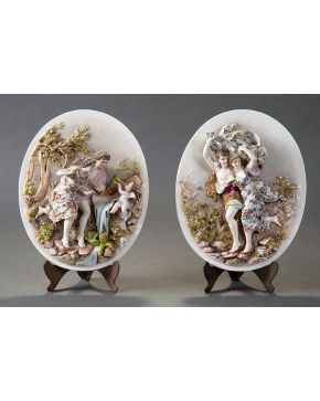 871-Decorativa pareja de medallones en porcelana centroeuropea con representación de escenas en altorelieve.  Medidas: 34x29 cm.
