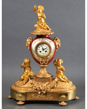 777-Reloj de sobremesa en bronce dorado y porcelana esmaltada, Francia, S.XIX sobre peana con decoraciones de niños en bulto redondo sujetando una guirnalda y remate de niño.