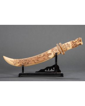 442-Daga, China ca.1900, en hueso tallado y pirograbado con cabeza de dragón en la empuñadura sobre peana de madera. Medida: 33,5 cm.
