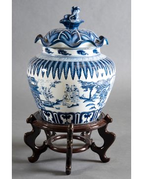 432-Tibor oriental en porcelana blanca y azul de paisajes y formas vegetales. Tapa ondulada con remate. Sobre peana tallada.  Altura: 38 cm 