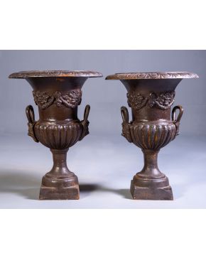 305-Pareja de jardineras de exterior en forma de copa en hierro con decoración de flores y guirnaldas. Cuerpo gallonado y asas con mascarone