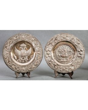326-Lote de dos platos españoles en plateado. Uno con escudo imperial y otro con florero en el campo y alas con decoración vegetal y roleos.