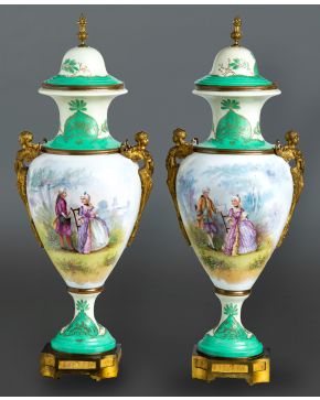 1024-Pareja de copas en porcelana de Sèvres con cuerpo de escenas galantes firmada y remates en verde y blanco con asas aladas en bronce dorado. Con m